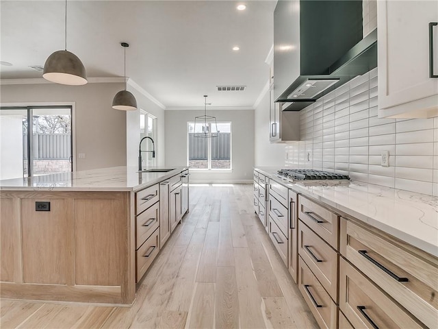 kitchen featuring light wood-type flooring, light stone counters, light brown cabinets, decorative light fixtures, and a large island