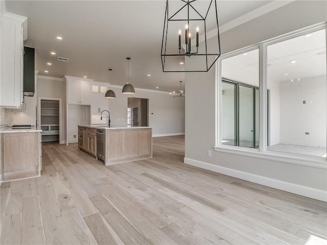 kitchen featuring hanging light fixtures, light hardwood / wood-style flooring, a large island with sink, crown molding, and white cabinets