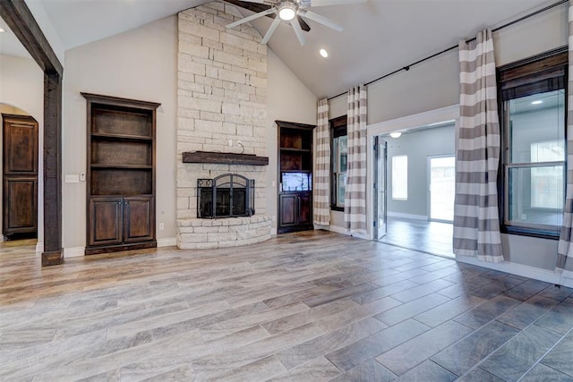 unfurnished living room with ceiling fan, a stone fireplace, high vaulted ceiling, and light hardwood / wood-style flooring