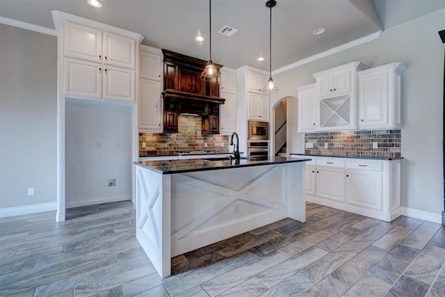 kitchen featuring white cabinets, backsplash, stainless steel appliances, and an island with sink