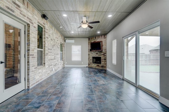 unfurnished living room with an AC wall unit, ceiling fan, brick wall, and a brick fireplace