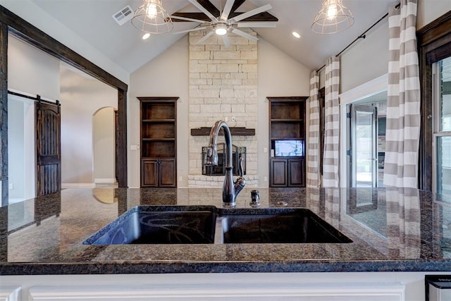 kitchen featuring dark stone counters, a barn door, sink, and hanging light fixtures