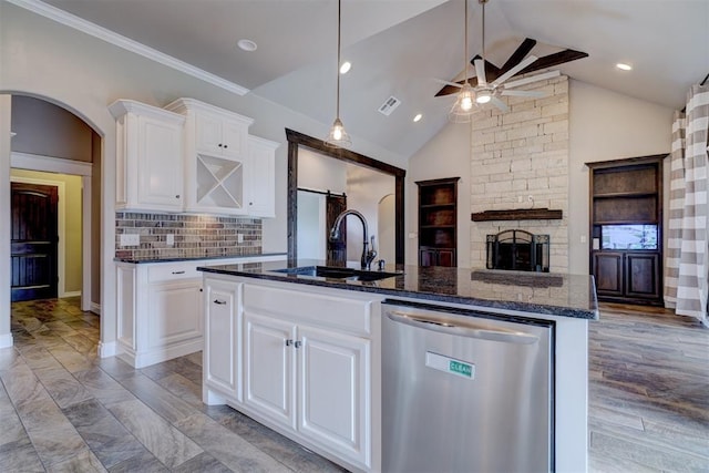 kitchen with dark stone countertops, white cabinetry, an island with sink, and stainless steel dishwasher