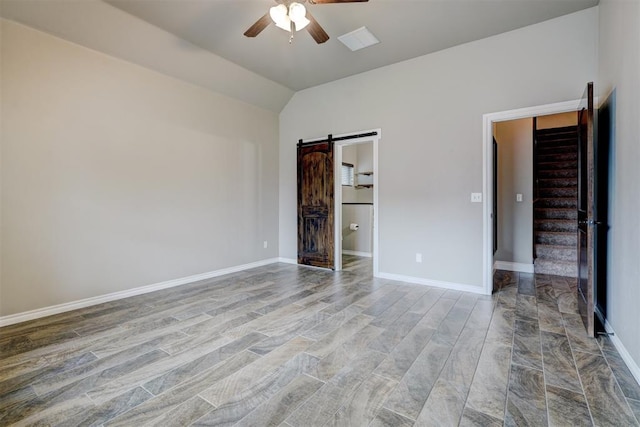 unfurnished room featuring light wood-type flooring, a barn door, vaulted ceiling, and ceiling fan