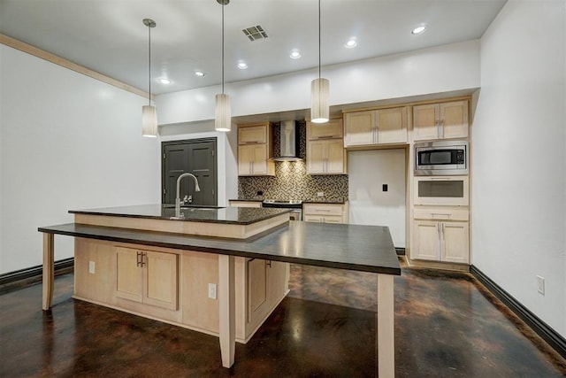 kitchen with sink, wall chimney range hood, an island with sink, pendant lighting, and appliances with stainless steel finishes