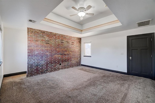 carpeted empty room featuring ceiling fan, brick wall, and a tray ceiling