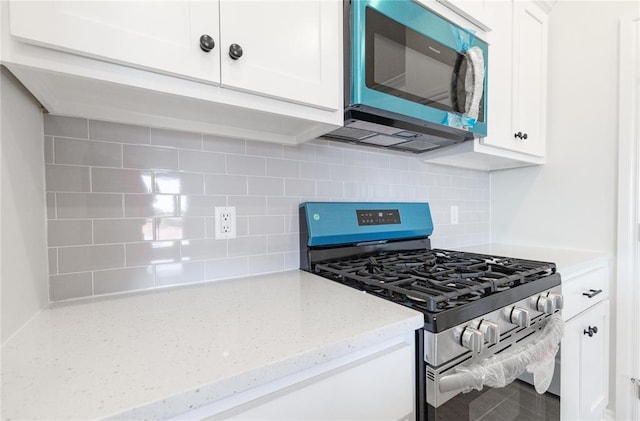 kitchen with light stone countertops, white cabinetry, gas stove, and decorative backsplash