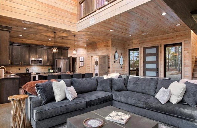 living room featuring sink, wooden ceiling, stacked washer / drying machine, and wood walls