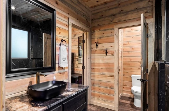 bathroom with vanity, toilet, wood-type flooring, and wooden walls