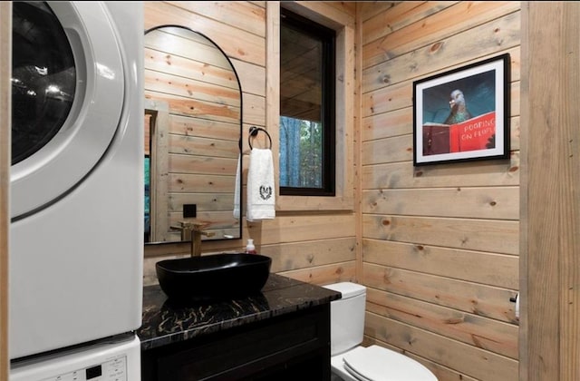 bathroom featuring toilet, stacked washer / drying machine, and wood walls