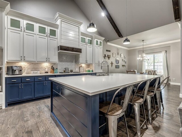 kitchen with white cabinets, lofted ceiling with beams, decorative light fixtures, and an island with sink