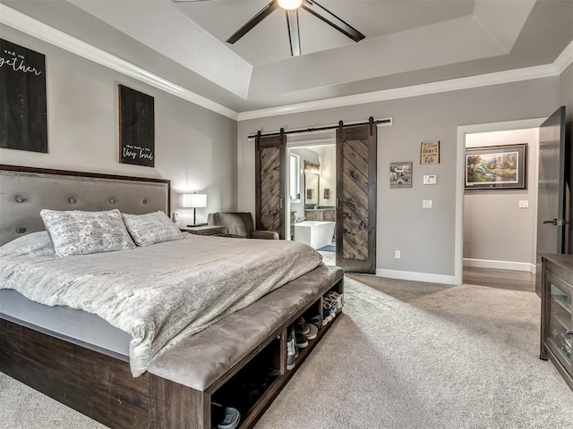 carpeted bedroom with ceiling fan, a barn door, a tray ceiling, and ensuite bath