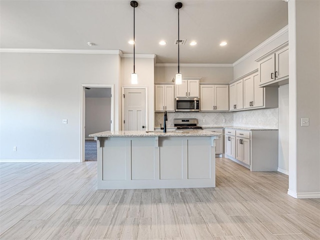 kitchen with light stone countertops, stainless steel appliances, hanging light fixtures, and an island with sink