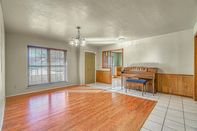 interior space featuring a textured ceiling, wooden walls, light hardwood / wood-style floors, and a notable chandelier