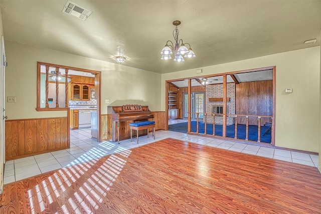 interior space featuring wood walls, light tile patterned floors, and ceiling fan with notable chandelier