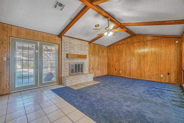 unfurnished living room with wooden walls, ceiling fan, light tile patterned floors, a fireplace, and a textured ceiling