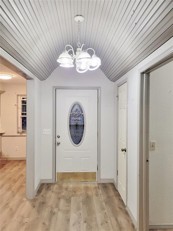 doorway with lofted ceiling, wooden ceiling, an inviting chandelier, and light hardwood / wood-style floors