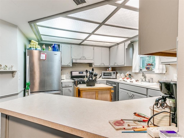 kitchen featuring appliances with stainless steel finishes, gray cabinetry, kitchen peninsula, and sink