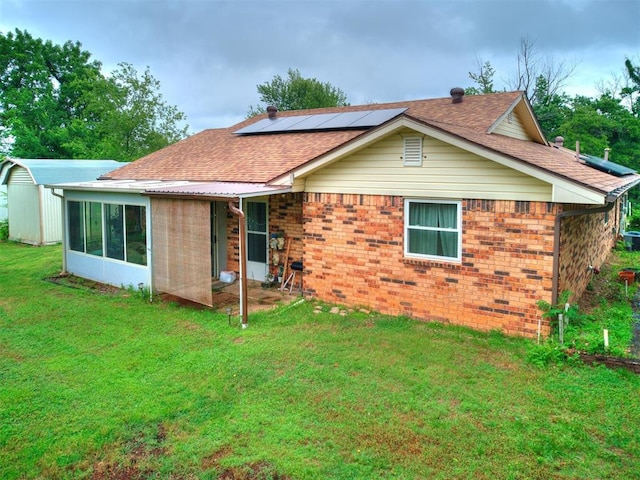 back of property featuring a sunroom, a yard, and solar panels