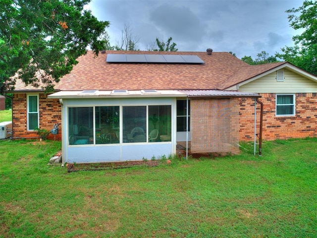 back of house featuring a sunroom, a lawn, and solar panels