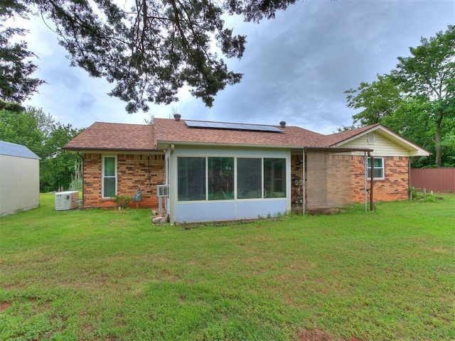 back of property with a yard, a sunroom, and solar panels