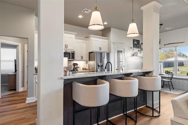 kitchen featuring a breakfast bar area, white cabinetry, light stone counters, kitchen peninsula, and stainless steel appliances