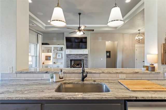 kitchen featuring dishwasher, a raised ceiling, sink, and a brick fireplace