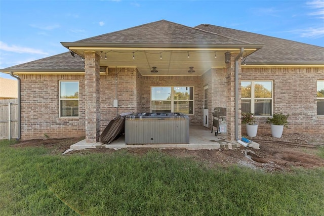 back of property with a hot tub, a patio, and a yard