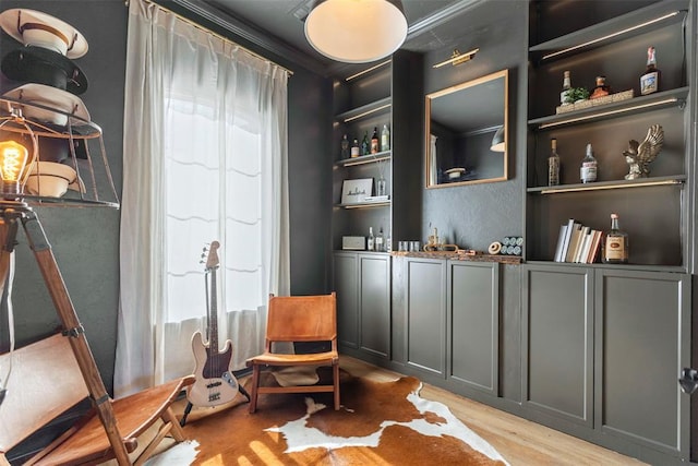 sitting room featuring built in shelves, crown molding, and light wood-type flooring