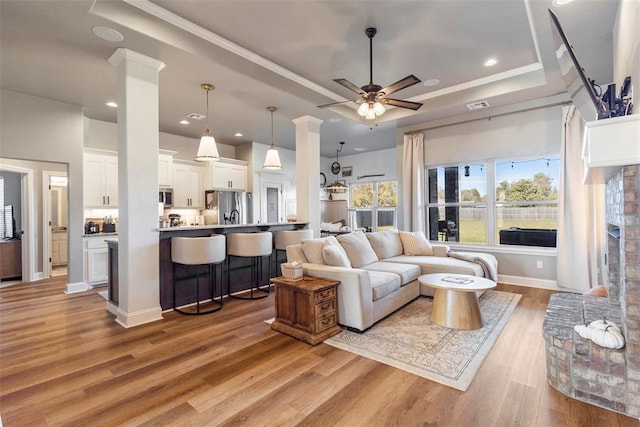 living room featuring a raised ceiling, ceiling fan, ornamental molding, and light wood-type flooring