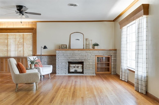 living room featuring a brick fireplace, light hardwood / wood-style flooring, ceiling fan, and crown molding