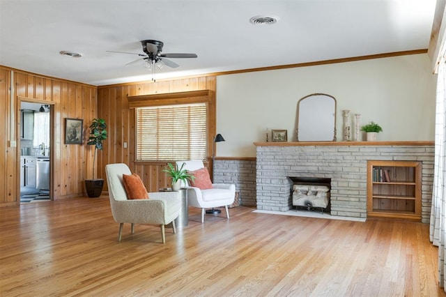 sitting room with ceiling fan, a brick fireplace, crown molding, wood walls, and light hardwood / wood-style floors