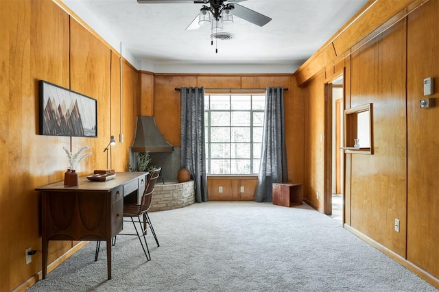 carpeted home office with ceiling fan and wood walls