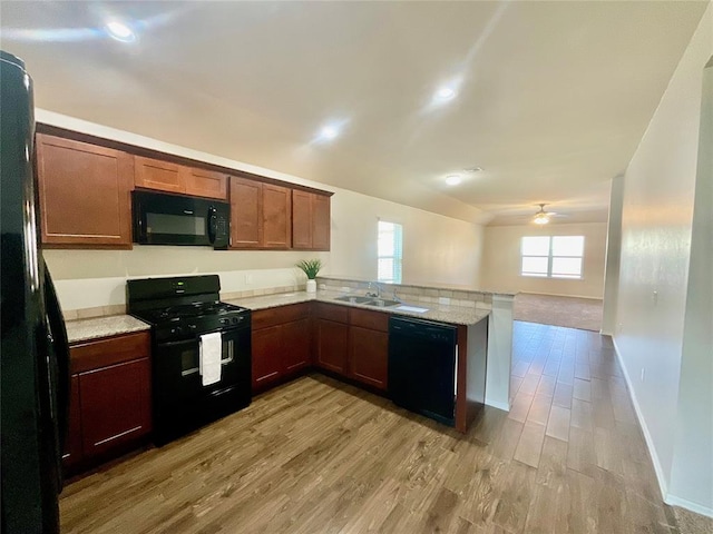 kitchen featuring kitchen peninsula, light stone counters, ceiling fan, black appliances, and light hardwood / wood-style floors