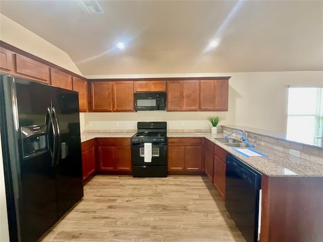 kitchen with light stone counters, kitchen peninsula, vaulted ceiling, black appliances, and light wood-type flooring