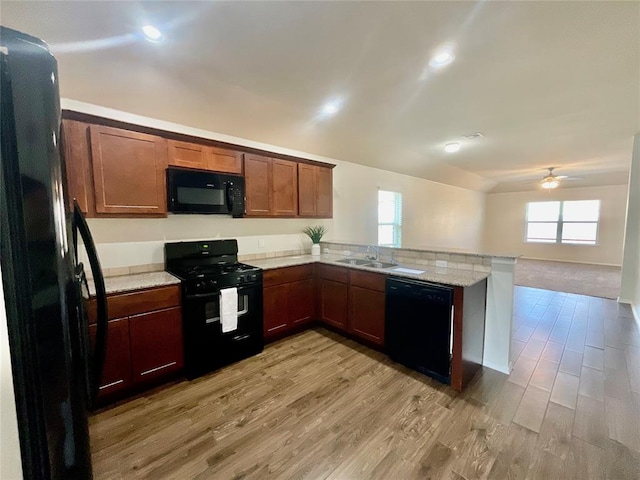 kitchen featuring kitchen peninsula, light wood-type flooring, light stone counters, sink, and black appliances