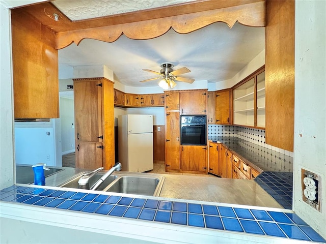 kitchen featuring tile countertops, black oven, white refrigerator, and ceiling fan