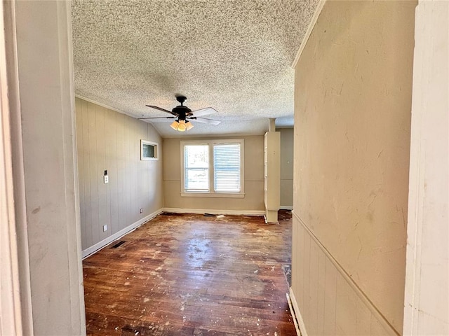 unfurnished room with ceiling fan, wooden walls, wood-type flooring, and a textured ceiling