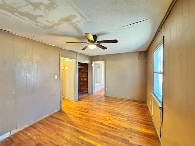 unfurnished room featuring light hardwood / wood-style floors, ceiling fan, and wood walls