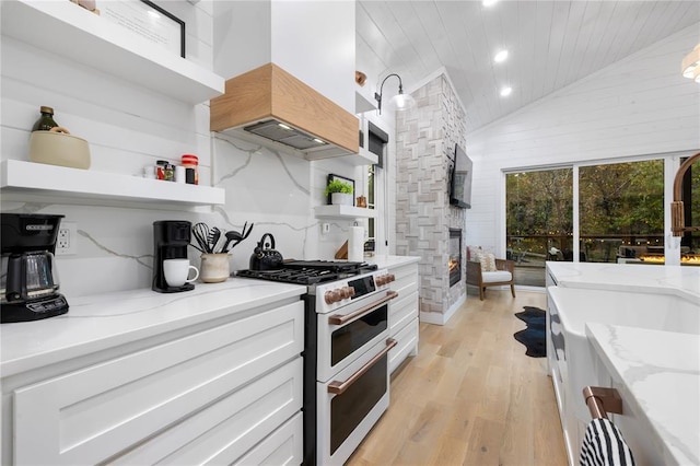 kitchen with light stone counters, white cabinets, range with two ovens, and custom exhaust hood