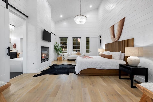 bedroom with a barn door, light hardwood / wood-style flooring, high vaulted ceiling, a notable chandelier, and a fireplace