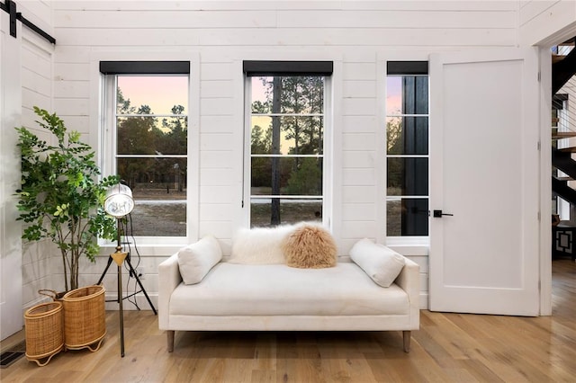 sitting room featuring a barn door, wooden walls, and light hardwood / wood-style flooring