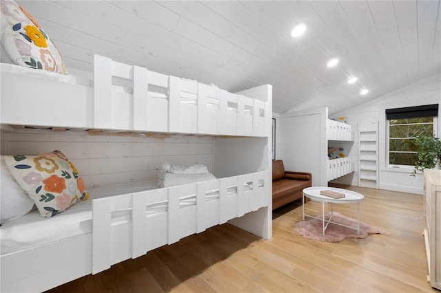 bedroom with wooden walls, light hardwood / wood-style flooring, wooden ceiling, and vaulted ceiling