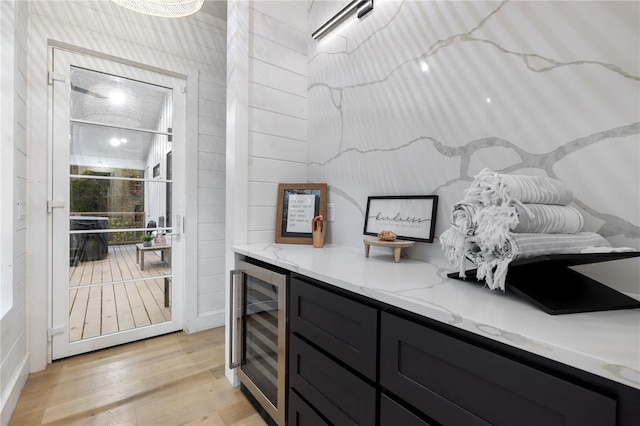 bar with light stone counters, beverage cooler, and light hardwood / wood-style floors