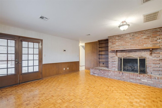 unfurnished living room featuring a brick fireplace, built in shelves, wood walls, and light parquet floors