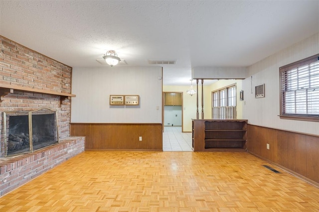 unfurnished living room with light parquet floors, a healthy amount of sunlight, a textured ceiling, and a brick fireplace