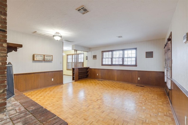 unfurnished living room featuring a textured ceiling, light parquet floors, and wooden walls