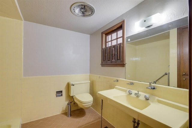 bathroom with tile patterned floors, toilet, tile walls, and a textured ceiling