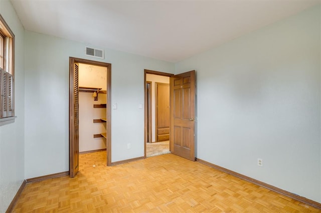 unfurnished bedroom with a closet, a walk in closet, and light parquet floors