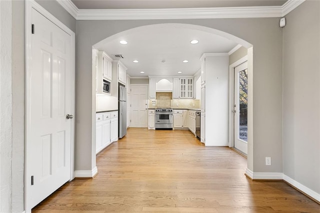 kitchen featuring white cabinets, light wood-type flooring, ornamental molding, appliances with stainless steel finishes, and tasteful backsplash